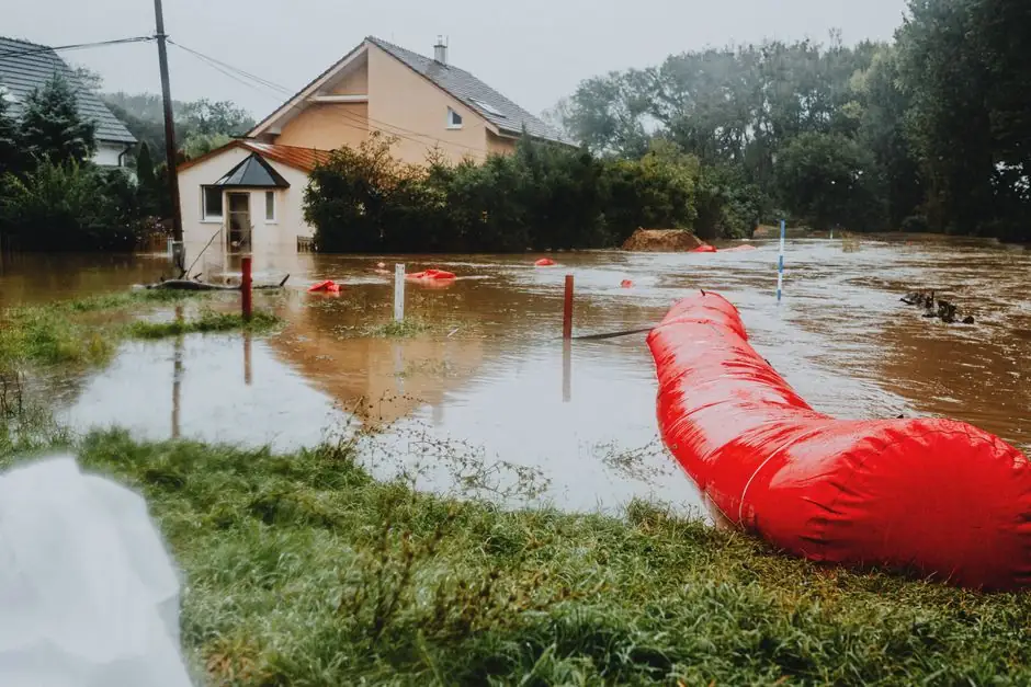 Flooded yard and homes with a red water barrier tube after heavy rain